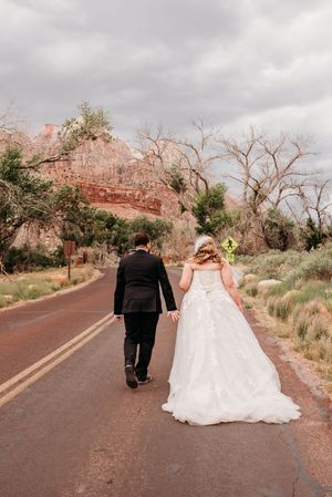 Bride and groom walking hand in hand down a scenic road in Zion National Park on their wedding day.
