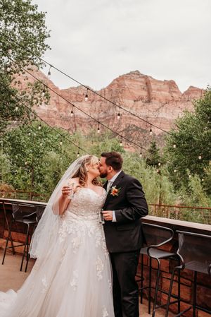 Bride and groom kissing on outdoor patio with red rock canyon views and string lights at Zion National Park wedding.