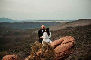 Couple sharing an intimate moment on red rocks with sweeping desert canyon views during their outdoor elopement ceremony.