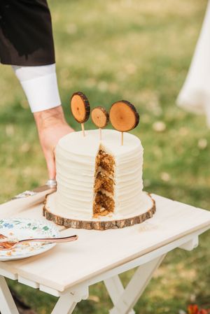 Rustic wedding cake with white frosting and wood slice toppers on a tree bark stand, with a slice cut out revealing layers.