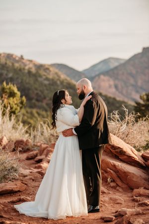 Bride and groom embrace at sunset with red rocks and mountain backdrop in an outdoor wedding portrait.