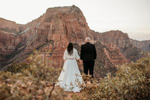 Bride and groom holding hands overlooking stunning red rock canyon formations at Zion National Park wedding.