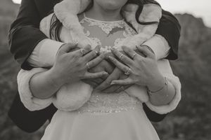 Black and white photo of a couple embracing a young flower girl, their hands clasped together over her white dress.