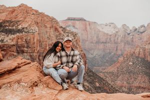 Couple smiling together on a red rock overlook at Zion National Park with dramatic canyon views.