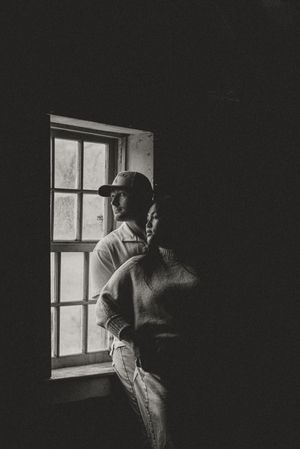 Couple embracing by a window in moody black and white portrait photography with dramatic lighting.