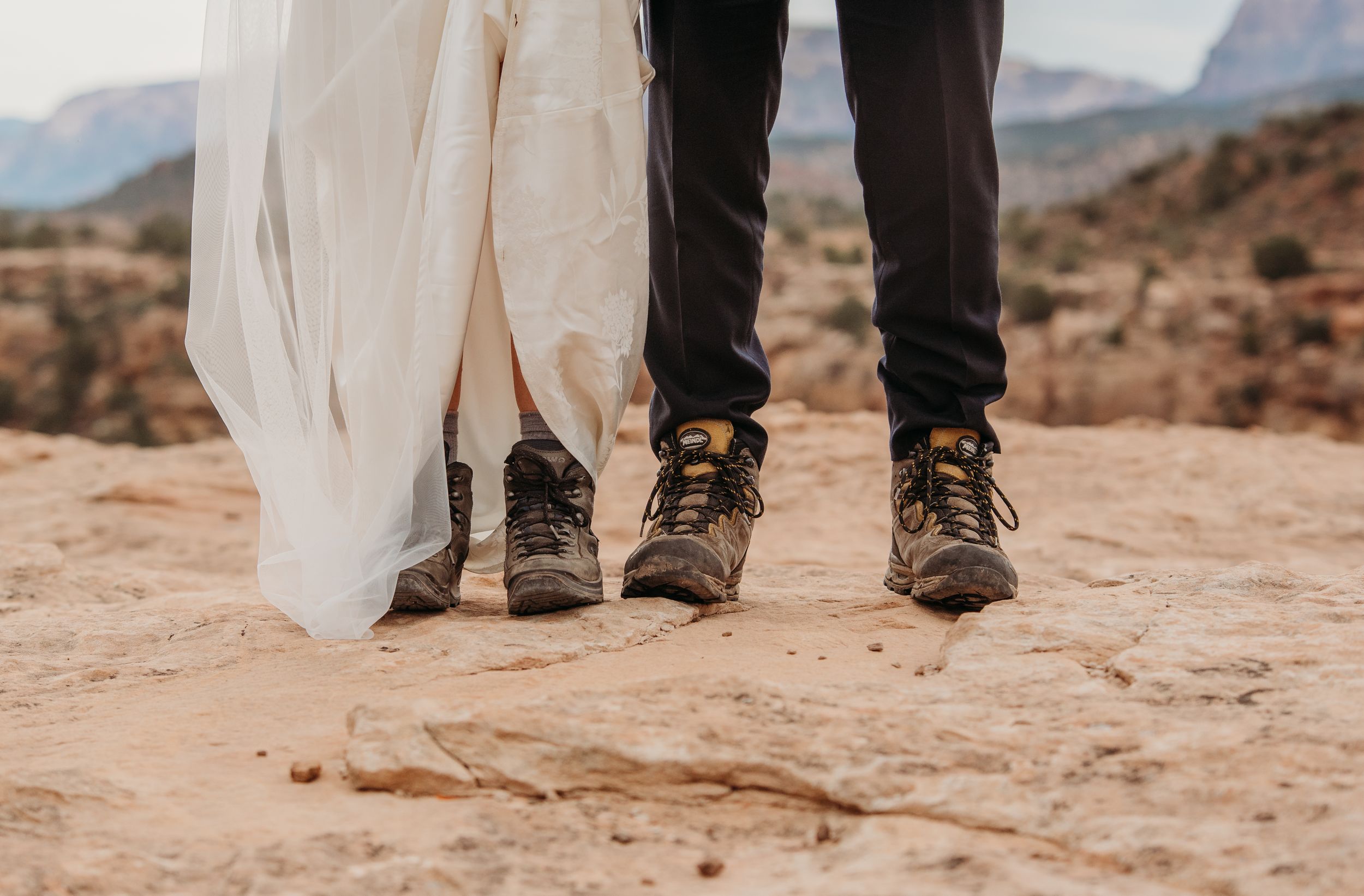 Bride and groom wearing matching hiking boots on red rock terrain in Sedona, Arizona desert wedding.