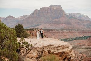 Couple elopes on a rocky cliff overlooking Zion National Park's stunning red rock canyon landscape.