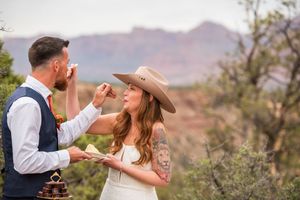 Bride and groom sharing wedding cake outdoors with red rock canyon landscape backdrop during desert elopement ceremony.