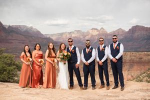 Wedding party poses at Grand Canyon overlook, bridesmaids in rust dresses, groomsmen in navy suits with vests.