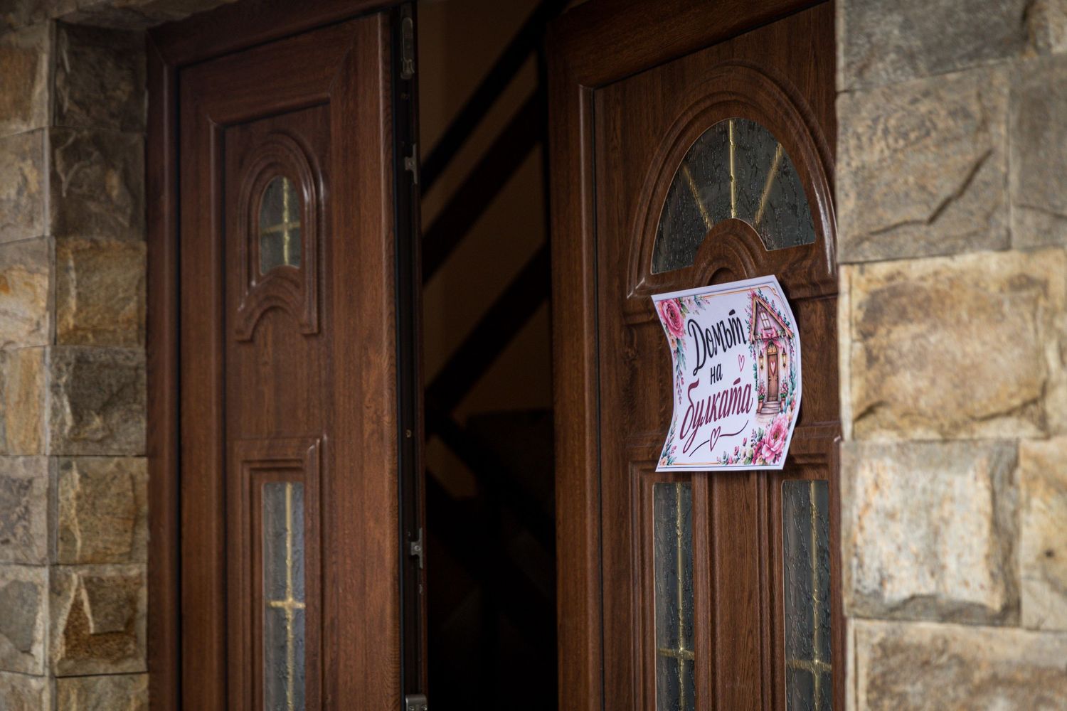 Wooden double doors with stone wall entrance featuring a decorative sign, rustic architecture exterior.