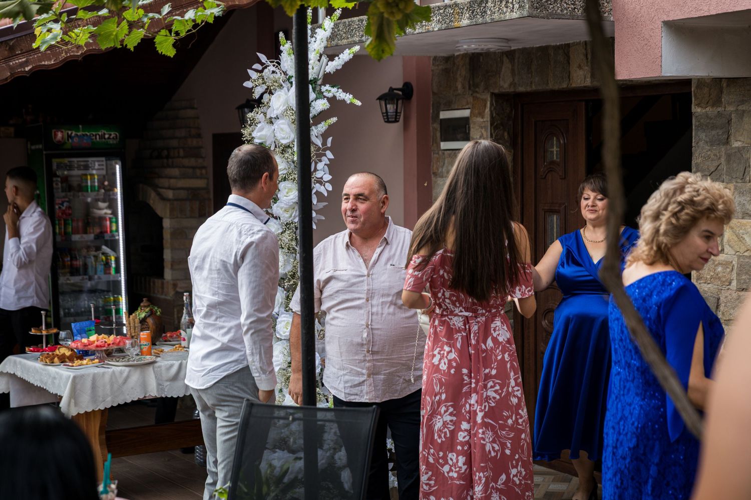 Group of elegantly dressed people socializing outdoors at a festive gathering near a decorated table.