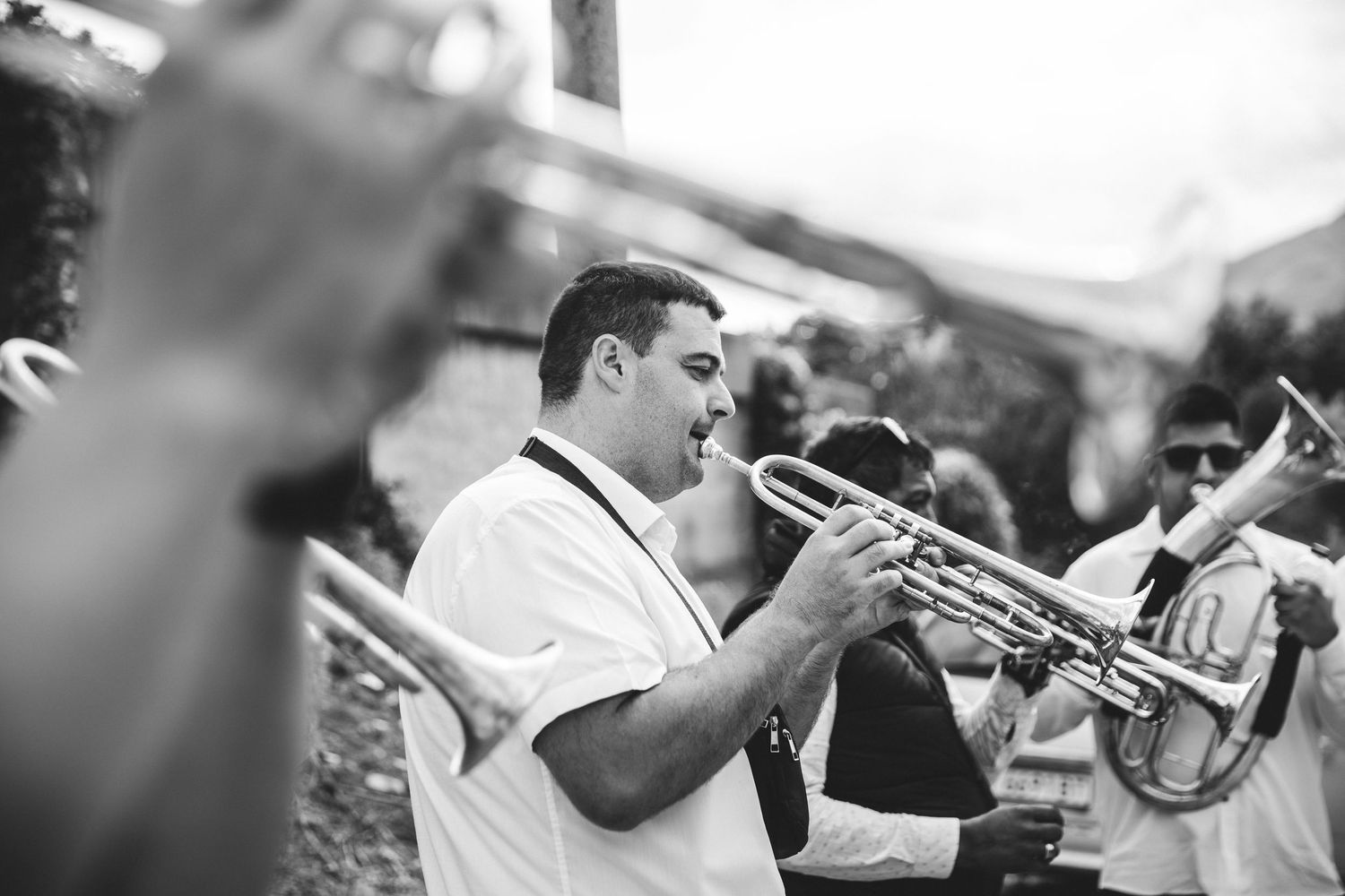 Black and white photo of a man playing trumpet in an outdoor brass band performance.