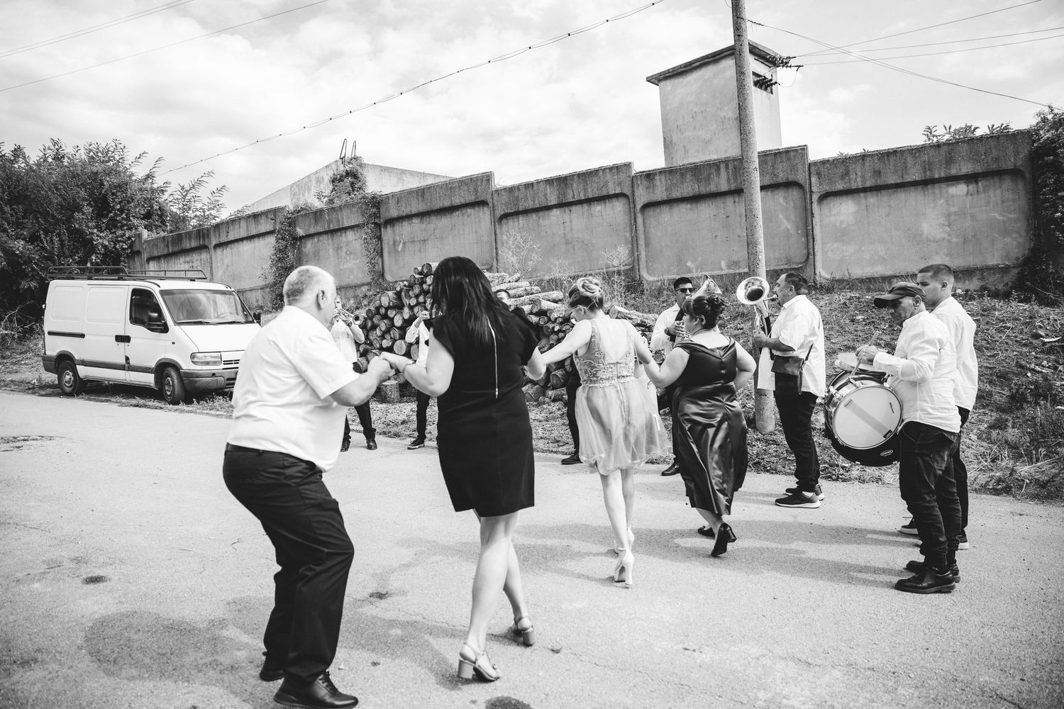 Black and white photo of people dancing in a street celebration with musicians playing drums and brass instruments outdoors.