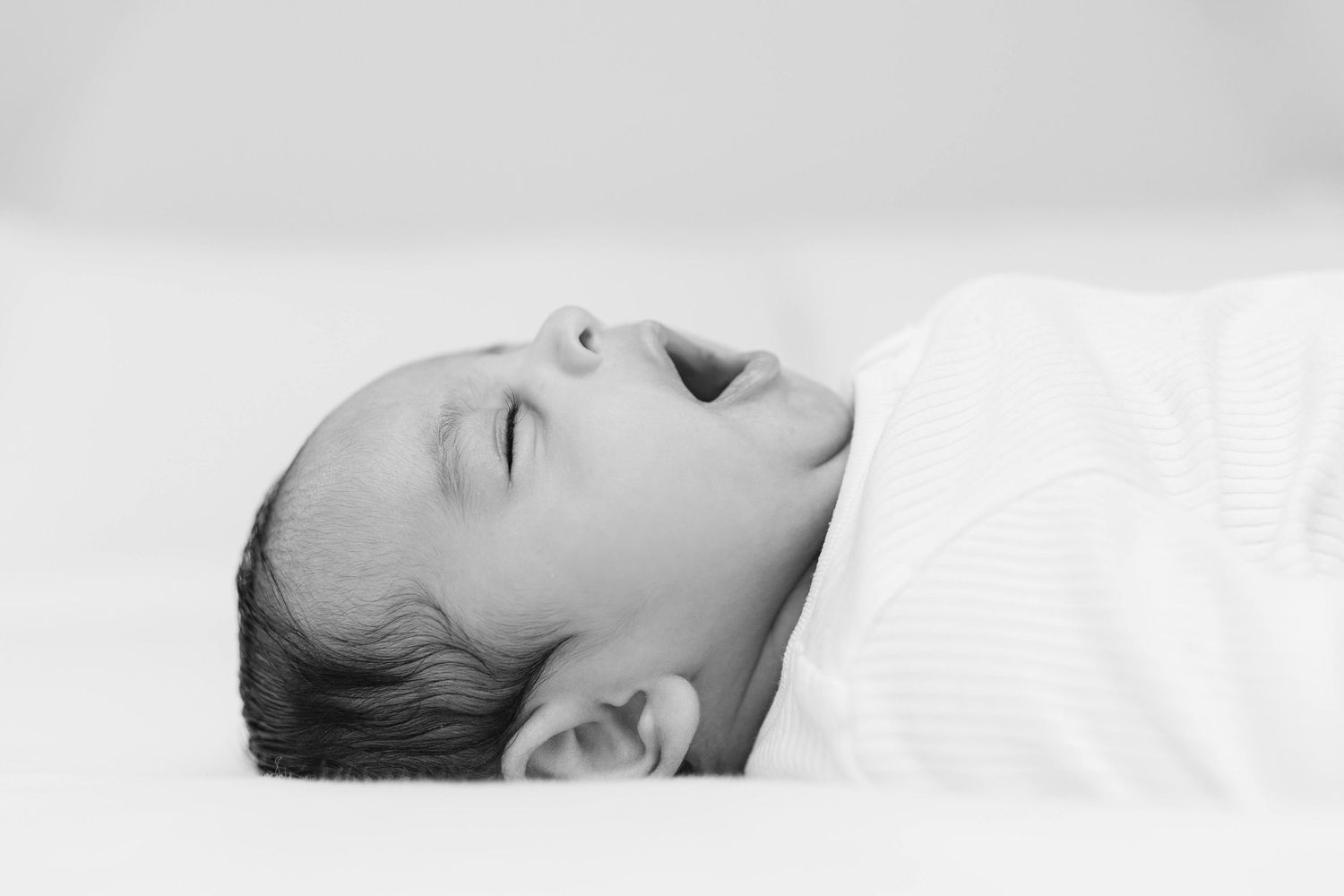 A couple tenderly holds their newborn baby by a bright window in a soft, light-filled room.