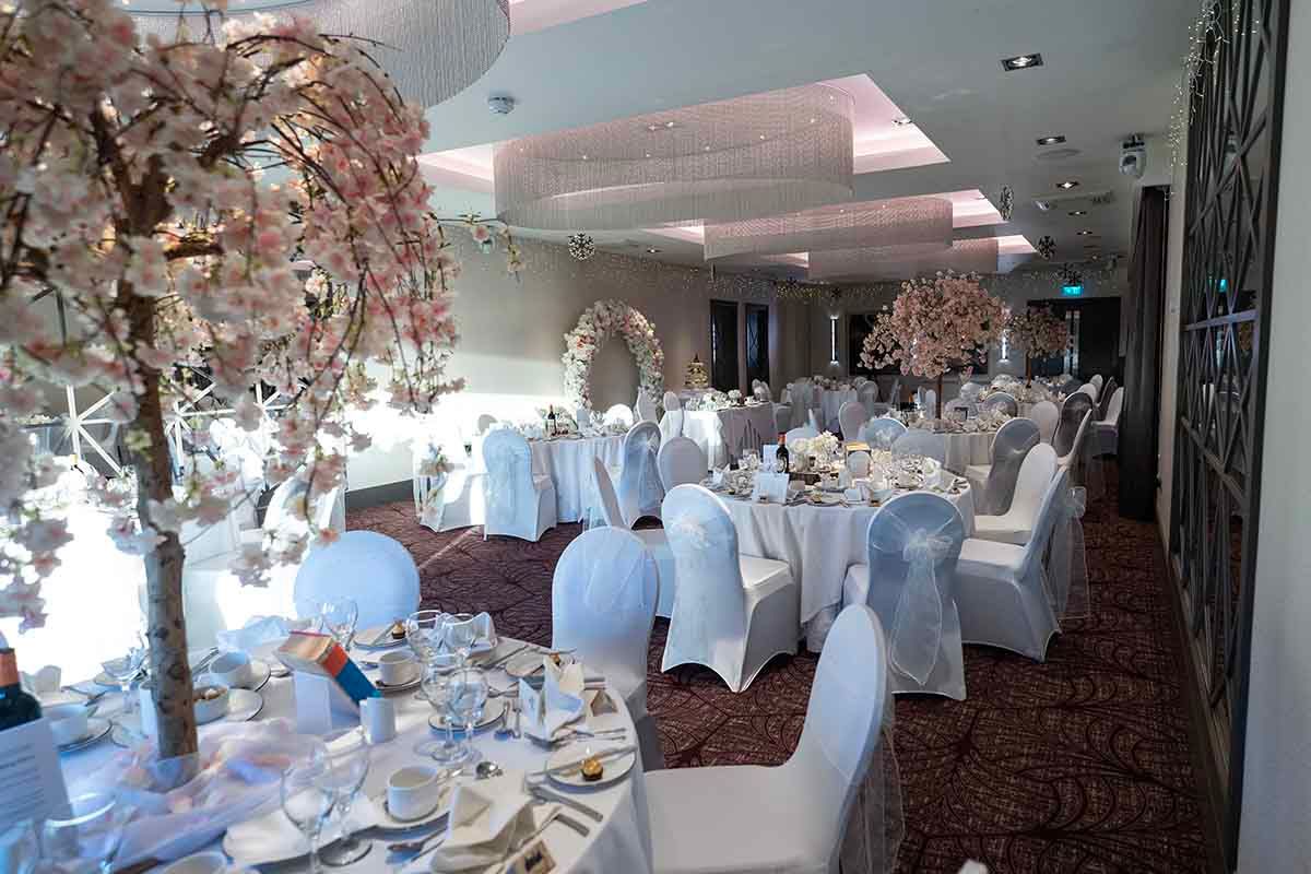 Elegant wedding reception hall with white chair covers, floral cherry blossom centerpieces, and beautifully set dining tables.