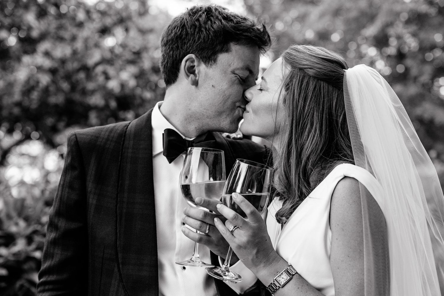 Black and white portrait of Beth and Matt kissing while holding champagne coupes.