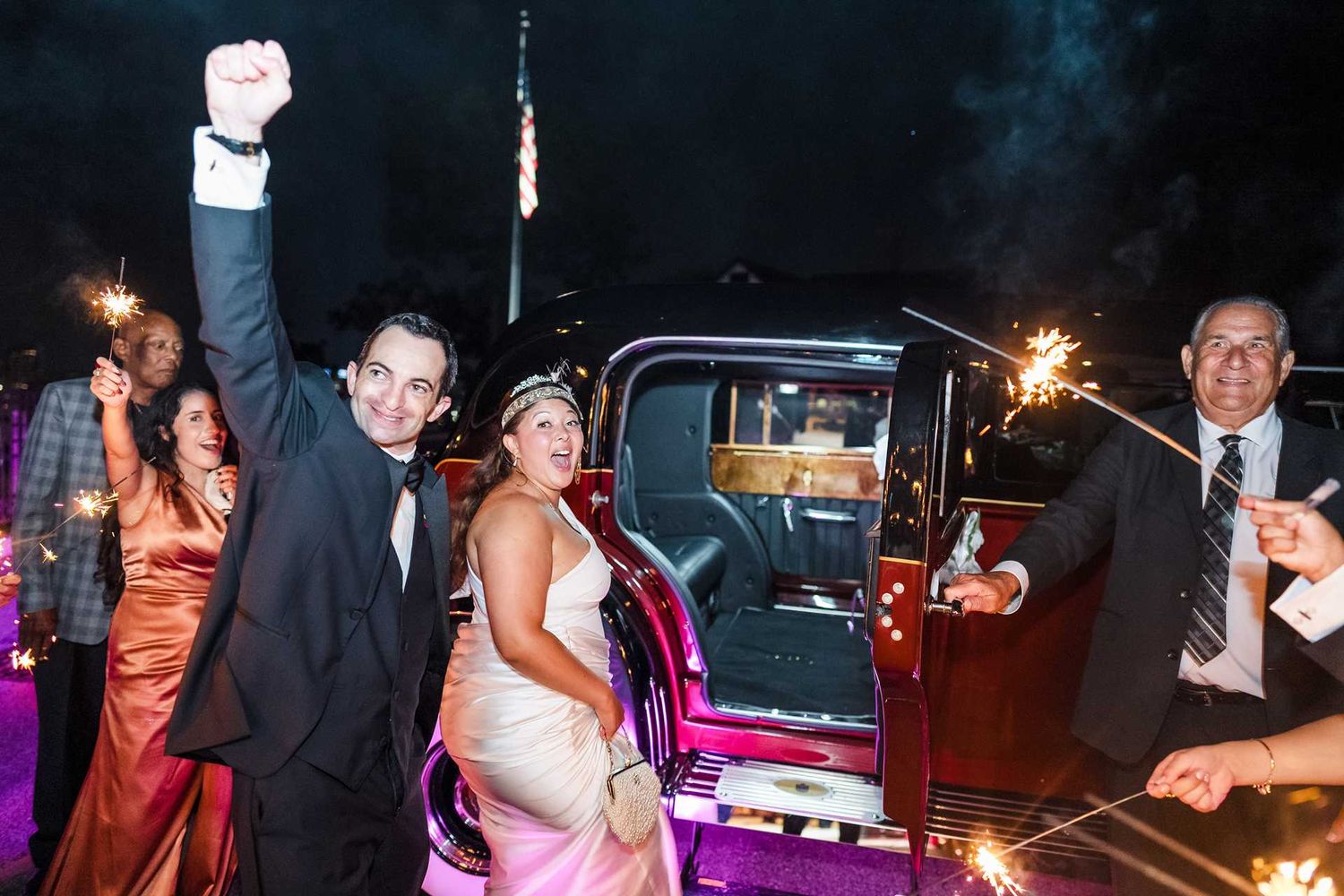 Newlyweds celebrate wedding exit with sparklers beside vintage car at night at the view wedding venue