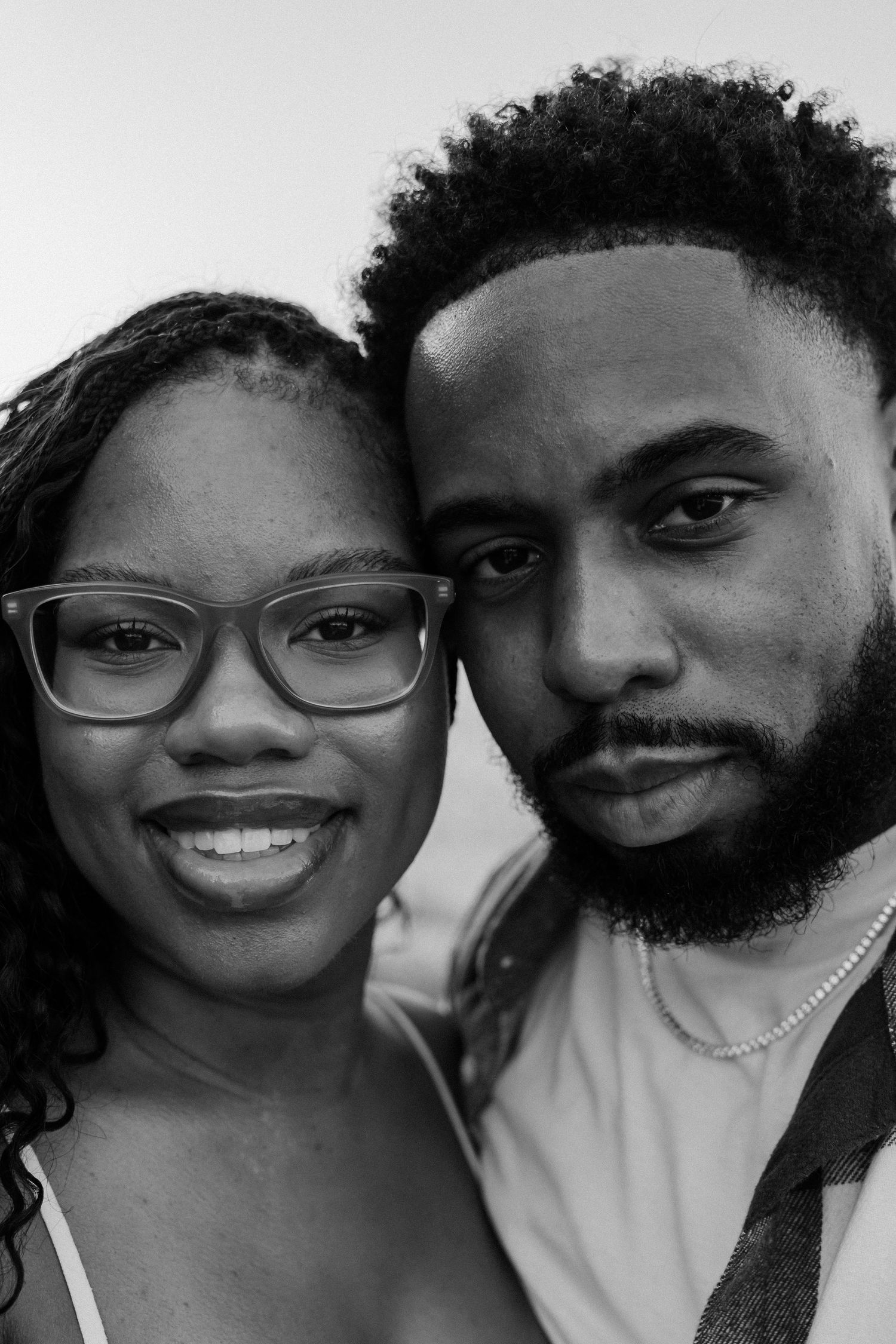 Black and white close-up portrait of a smiling woman with glasses and a bearded man posing together outdoors.