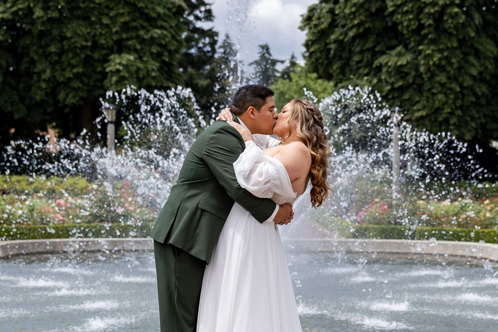 Bride and groom share a romantic kiss in front of a garden fountain on their wedding day.