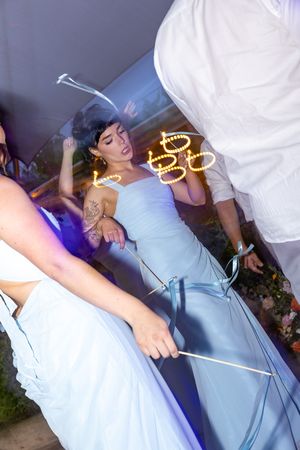 Bridesmaid in light blue gown dancing with sparklers at a wedding reception celebration.