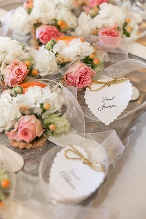 Elegant wedding favor boxes with heart tags beside pink and white floral arrangements on a silver tray.
