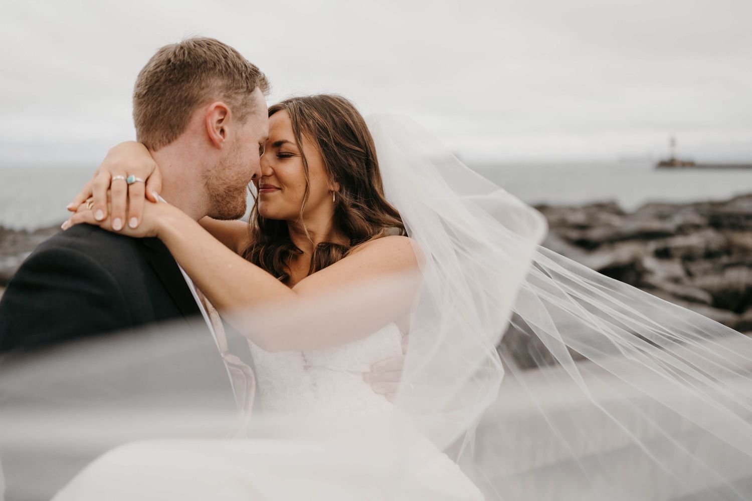 Bride and groom embrace romantically among lush green vineyard rows under a bright blue sky on their wedding day.