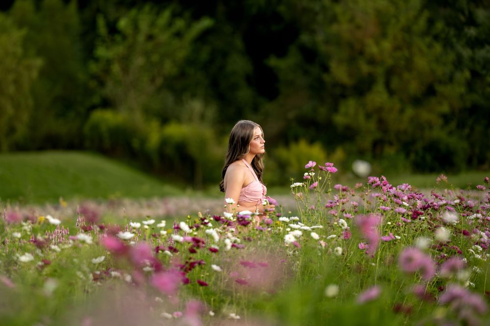Woman in pink dress sitting peacefully among pink and white cosmos flowers in a lush garden.