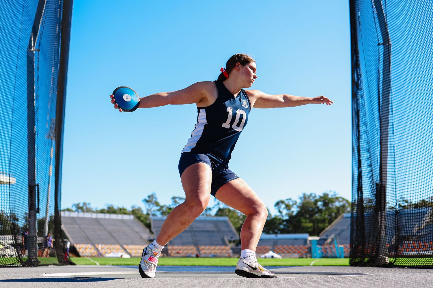 Female athlete wearing number 10 jersey throws discus on track field under clear blue sky.