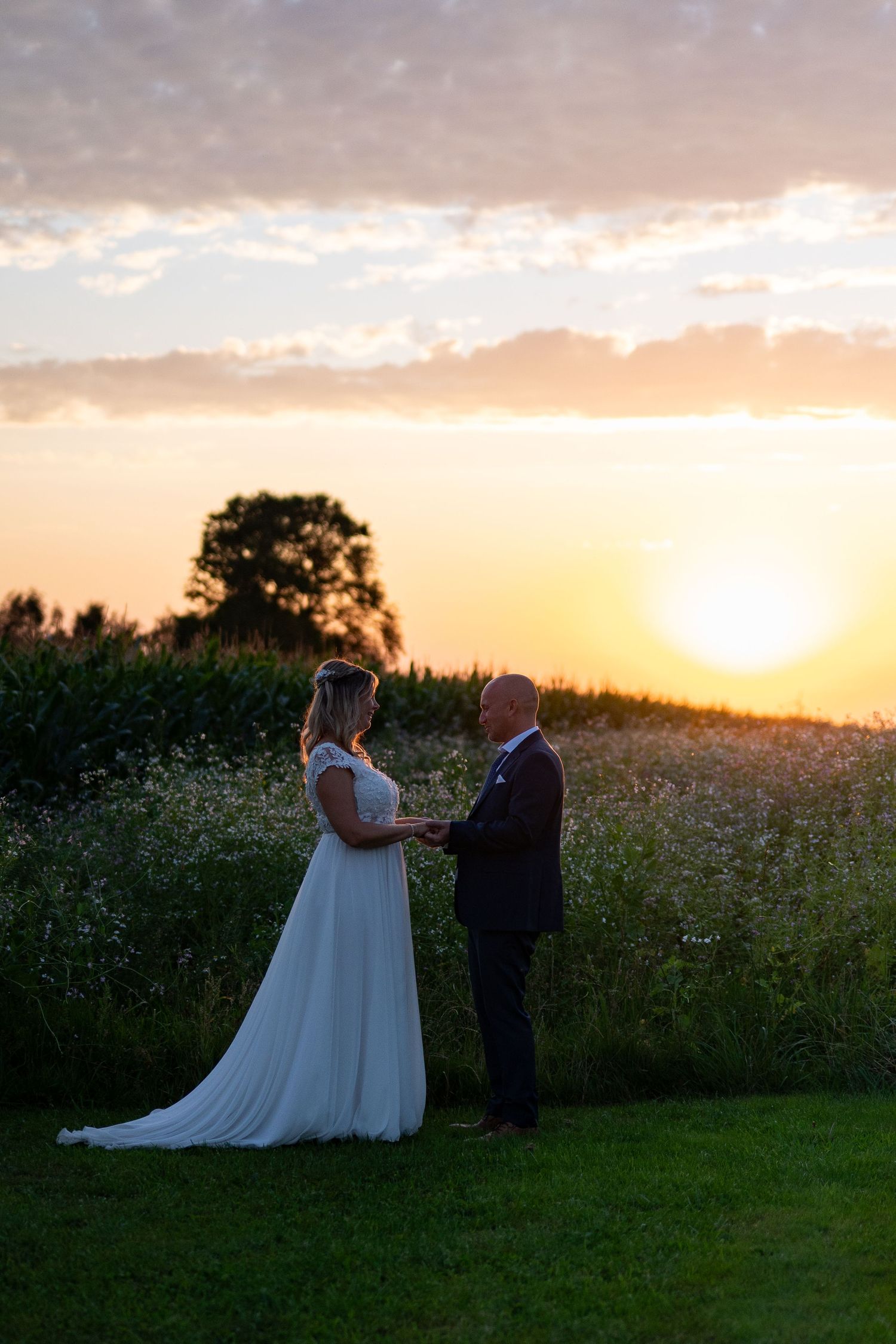 Bride and groom hold hands at sunset in a field of wildflowers, golden light illuminating their outdoor wedding ceremony.