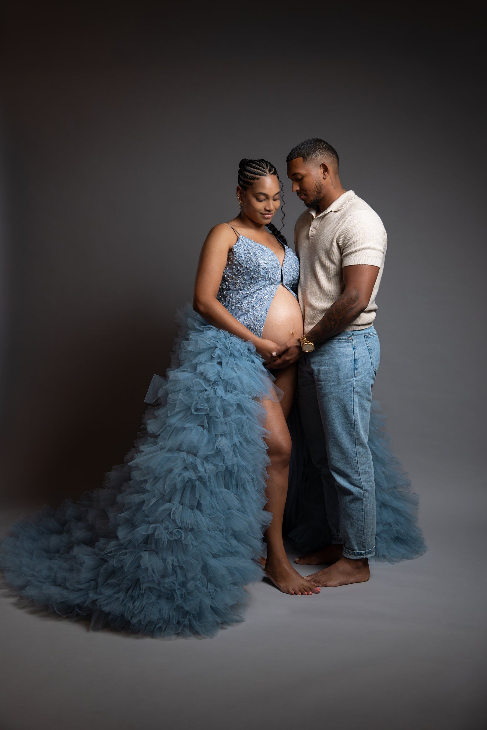 Pregnant woman in blue tulle gown with partner in studio maternity photo shoot.