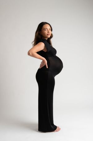 Pregnant woman in black maxi dress posing sideways, showcasing baby bump in professional maternity photo shoot.