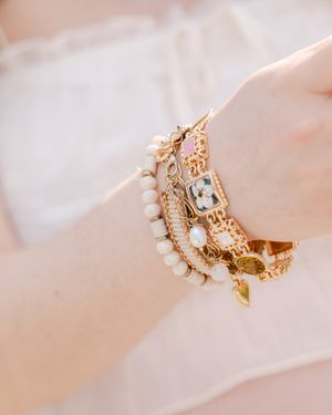 Stacked gold and pearl bracelets with charm details on a wrist, featuring elegant floral and heart accents.