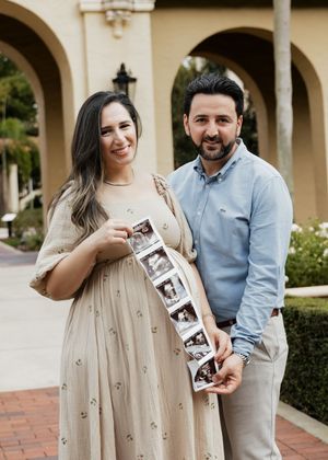 Pregnant woman in floral dress holds ultrasound strip with partner during maternity announcement photo shoot outdoors.
