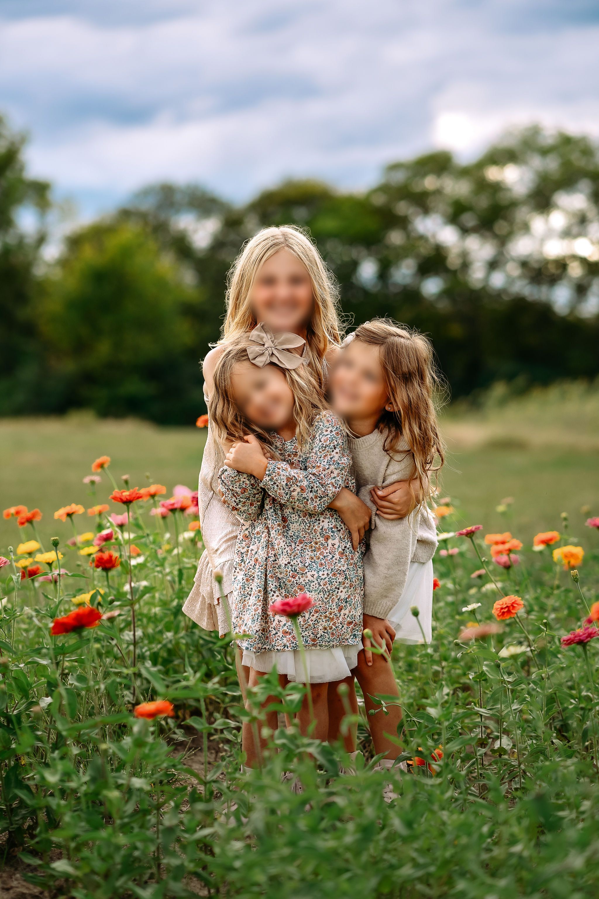 Three sisters wearing coordinated cream knits and a muted floral dress in a flower field in Middle Tennessee.