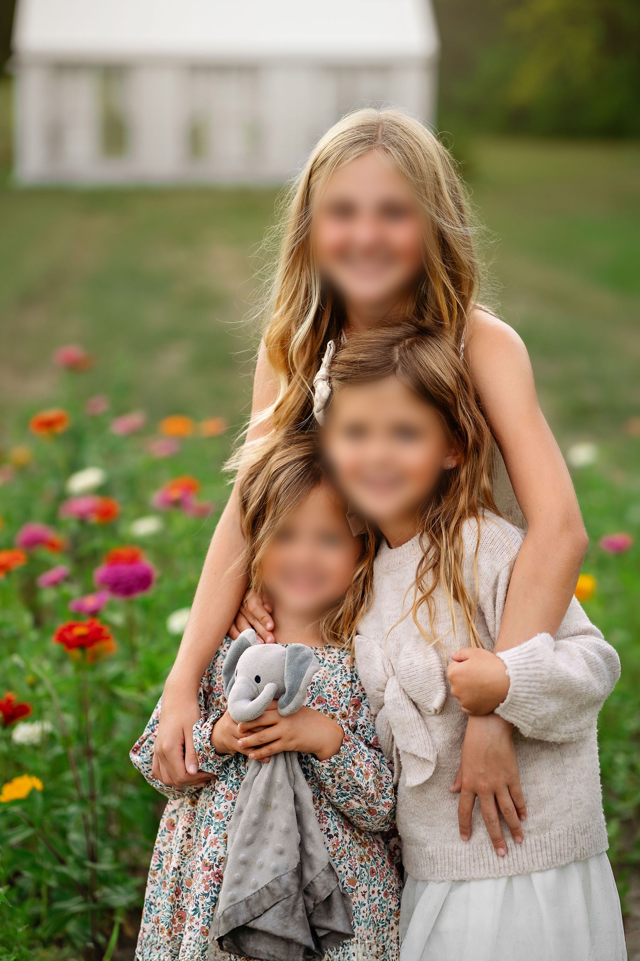 Three sisters wearing coordinated cream knits and a muted floral dress in a flower field in Middle TN.