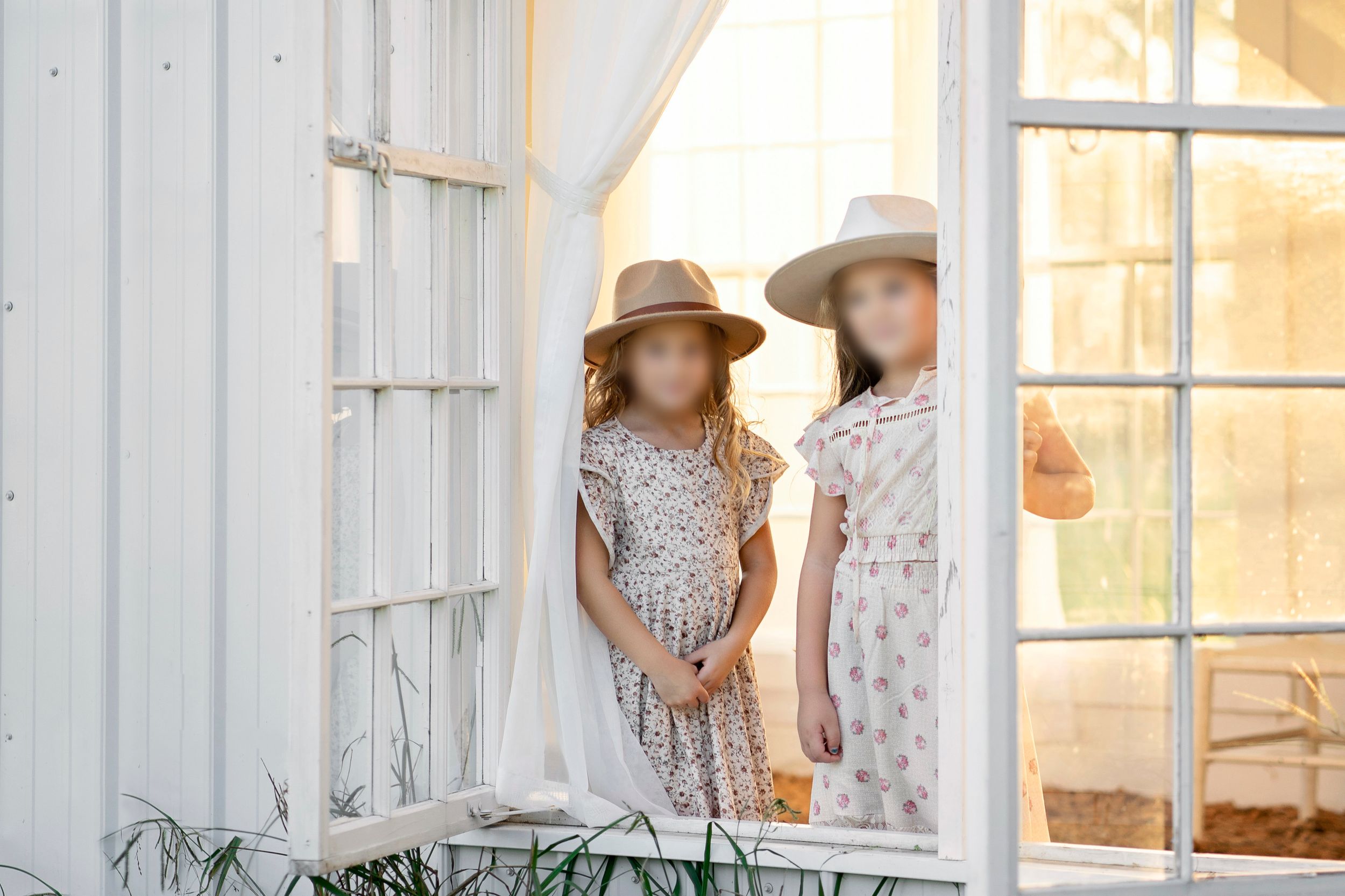 Two girls in flowing floral dresses and neutral hats during a Middle Tennessee golden-hour boho session at South 40 farm.