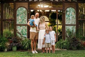 Family wearing cream, soft blue, and khaki outfits outside a garden greenhouse.