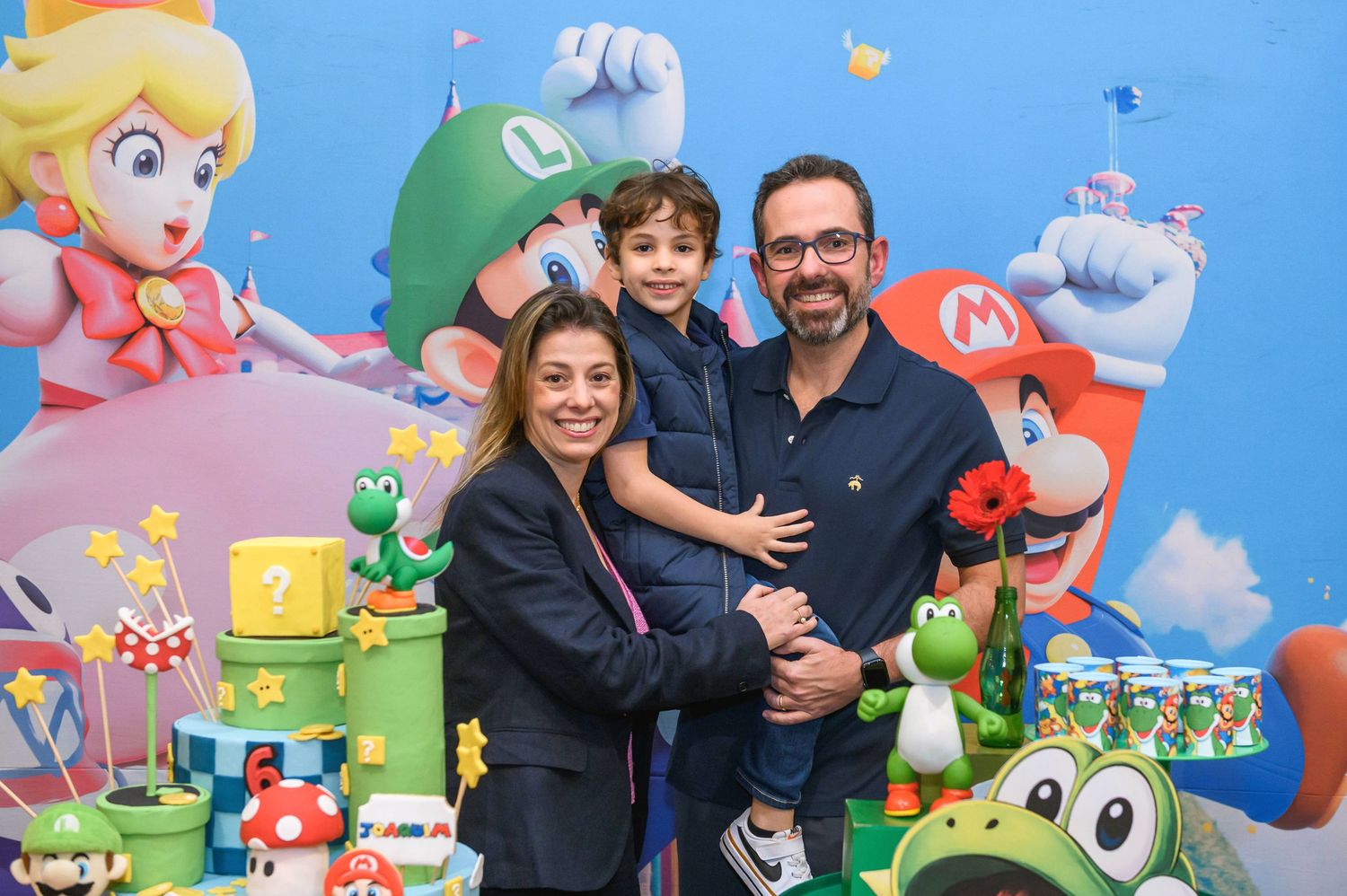 Family posing at a Super Mario Bros themed birthday party with colorful decorations and character backdrop.