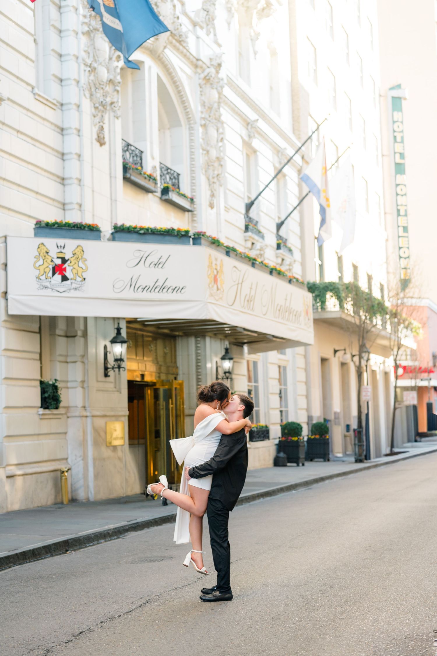 A groom lifts his bride outside Hotel Monteleone in New Orleans, sharing a romantic kiss on the street.