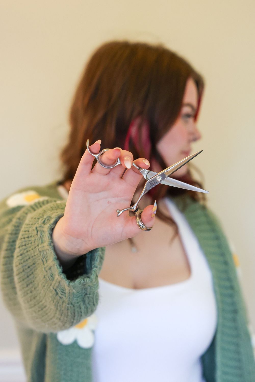 Woman in green cardigan holding professional hair scissors toward camera in a salon setting.