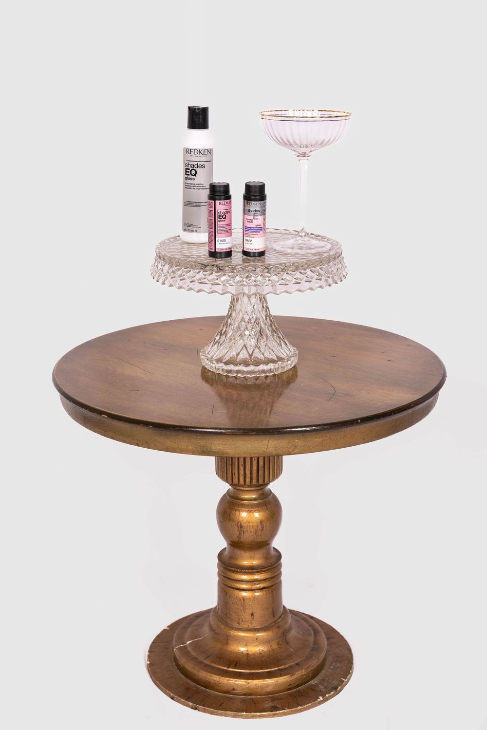 Elegant gold pedestal table with crystal cake stand holding hair care products and a martini glass.