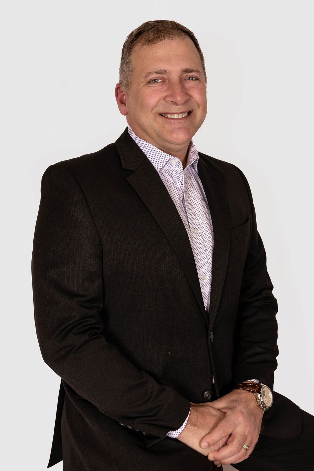 Smiling middle-aged man in dark blazer and light pink shirt, professional headshot photo against white background.