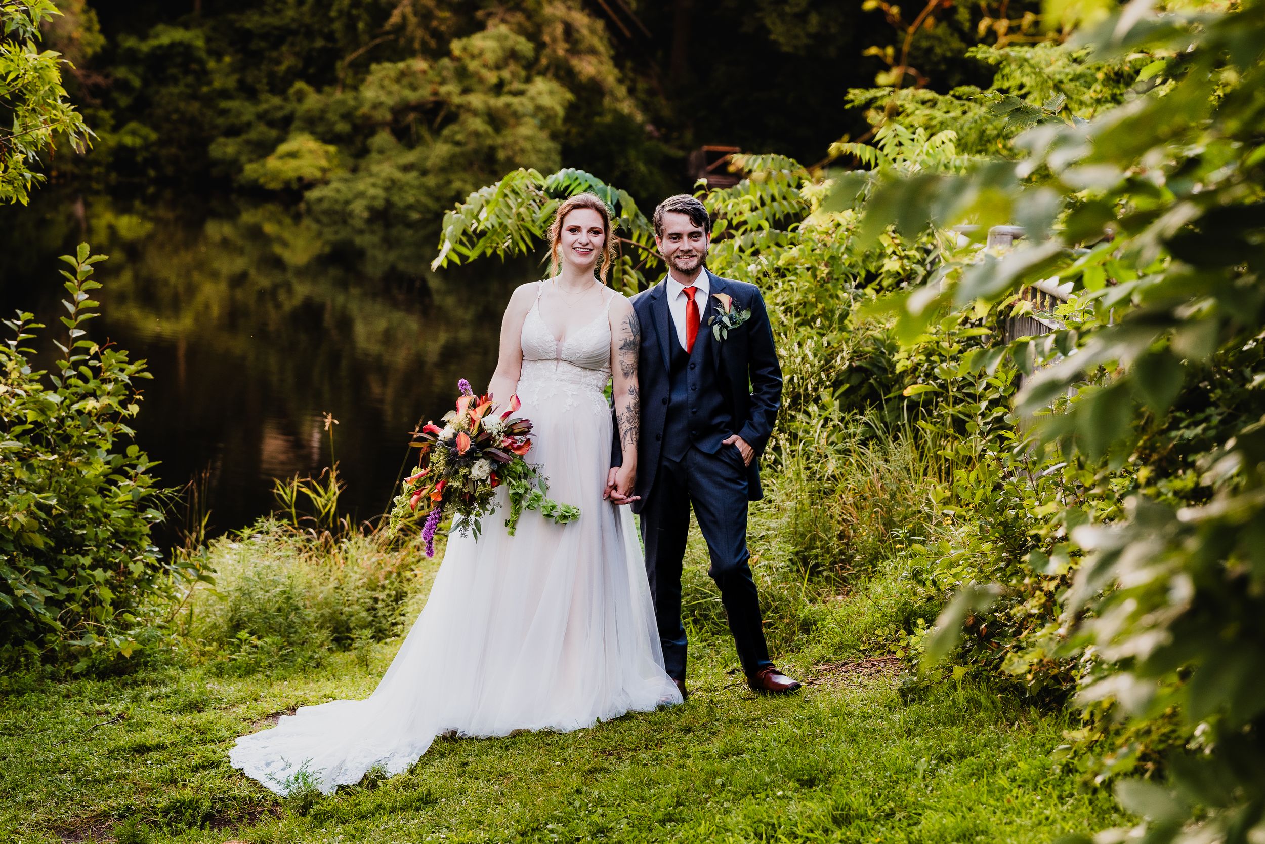 Newlywed couple poses in front of a lush green garden backdrop during their outdoor summer wedding celebration.