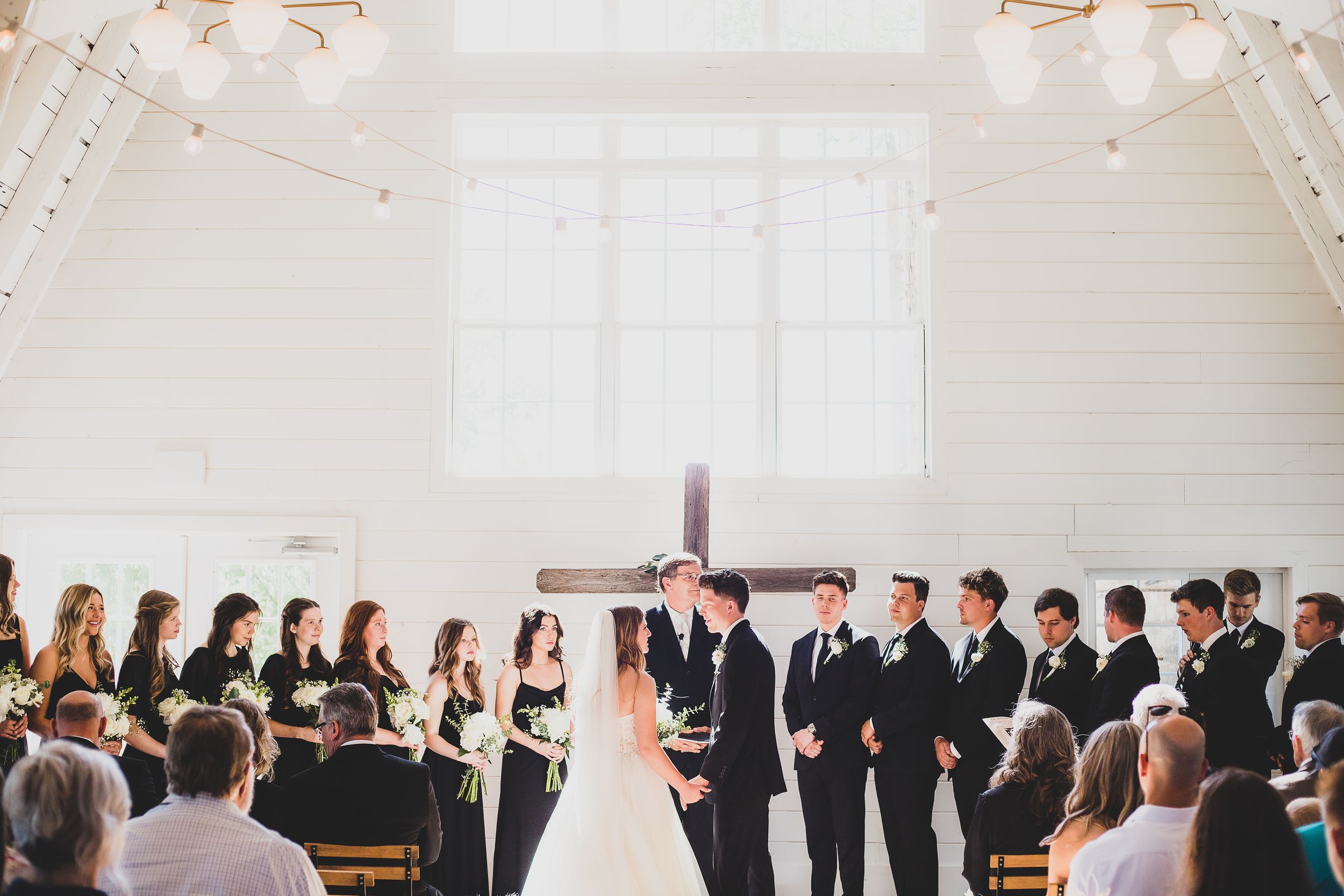 A light filled church wedding ceremony with guests seated in wooden pews while the wedding party stands at the altar.