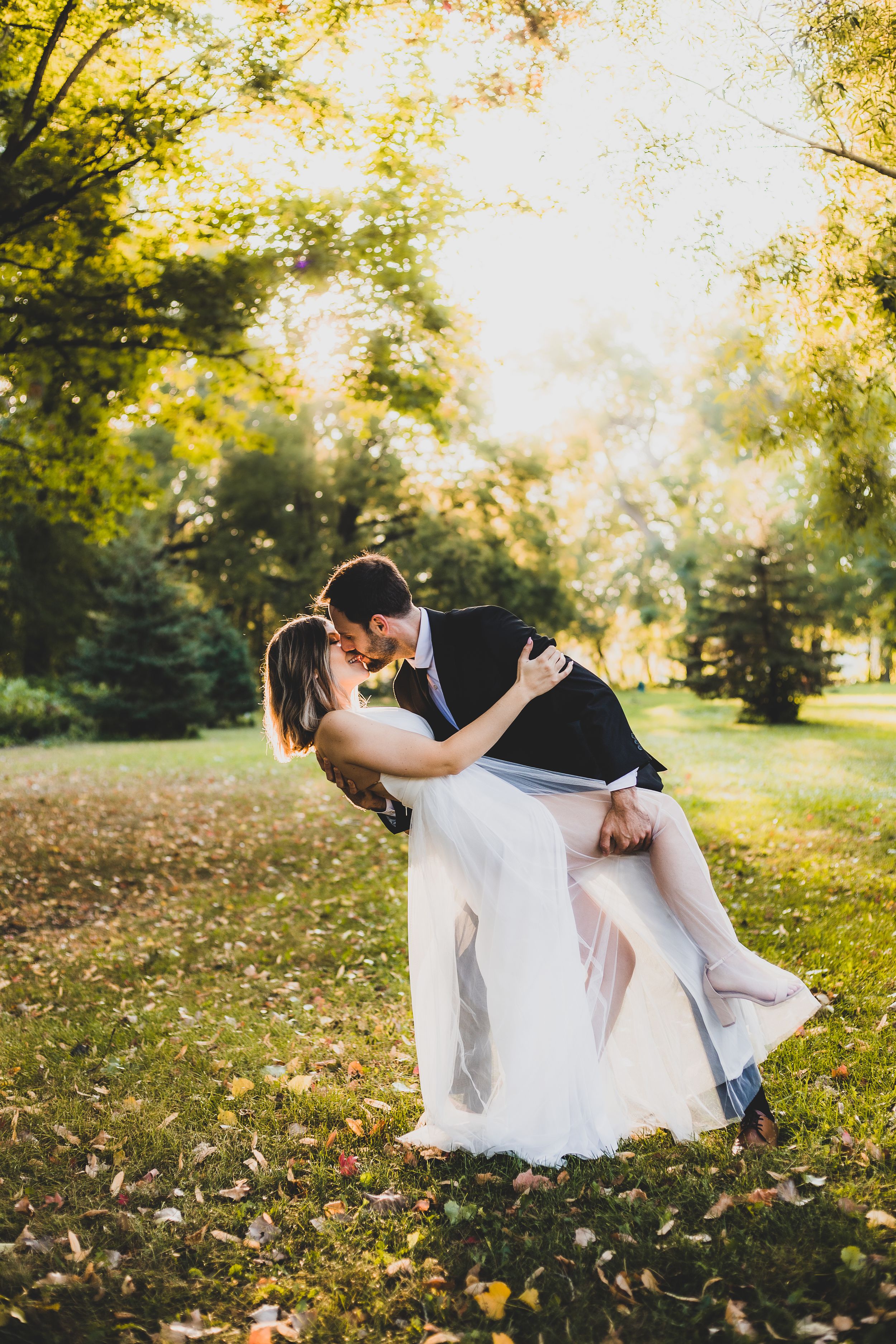 Dramatic dip pose in autumn park with sunlight filtering through golden leaves.