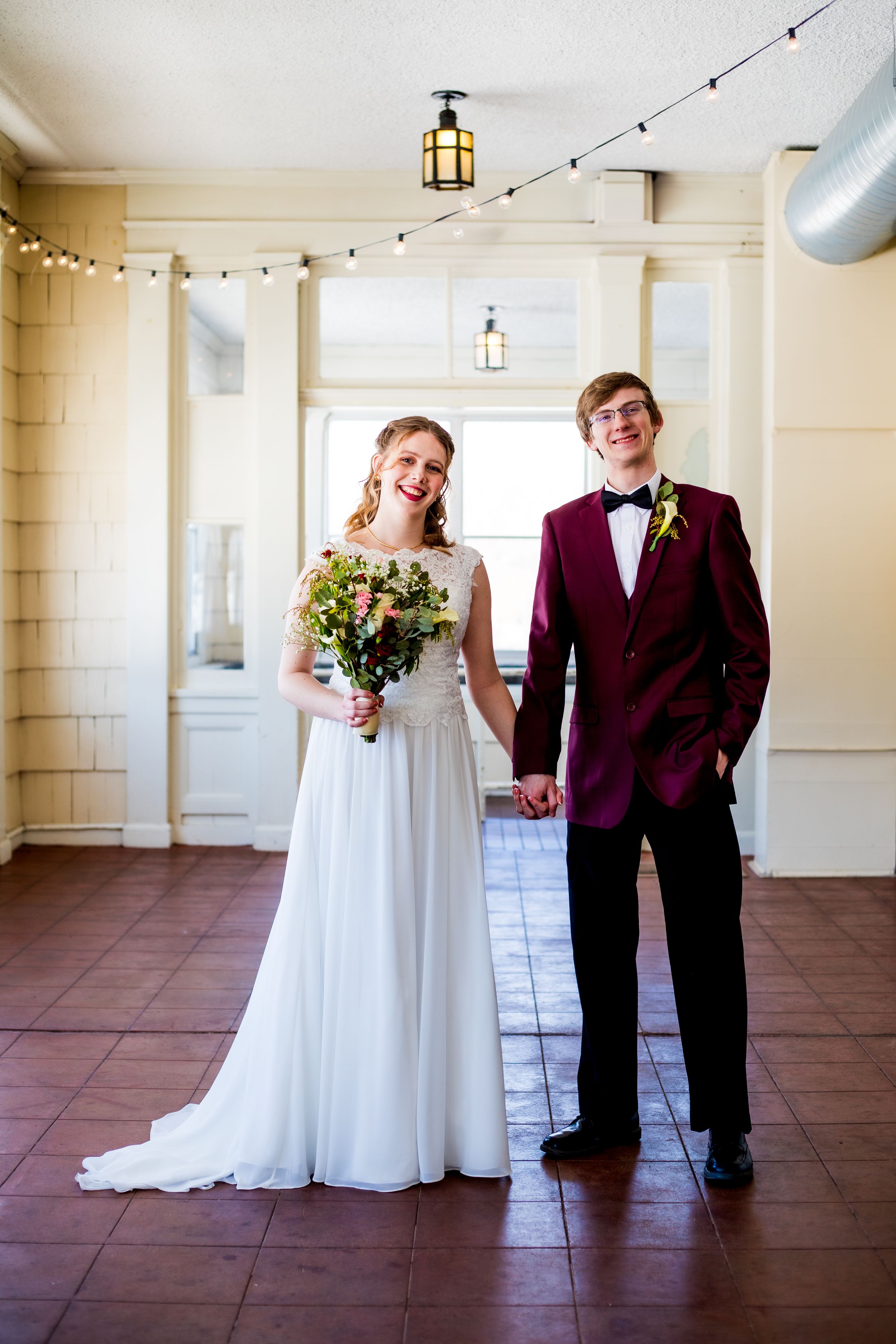 A couple in wedding attire share a happy moment in a vintage interior with string lights and lanterns.