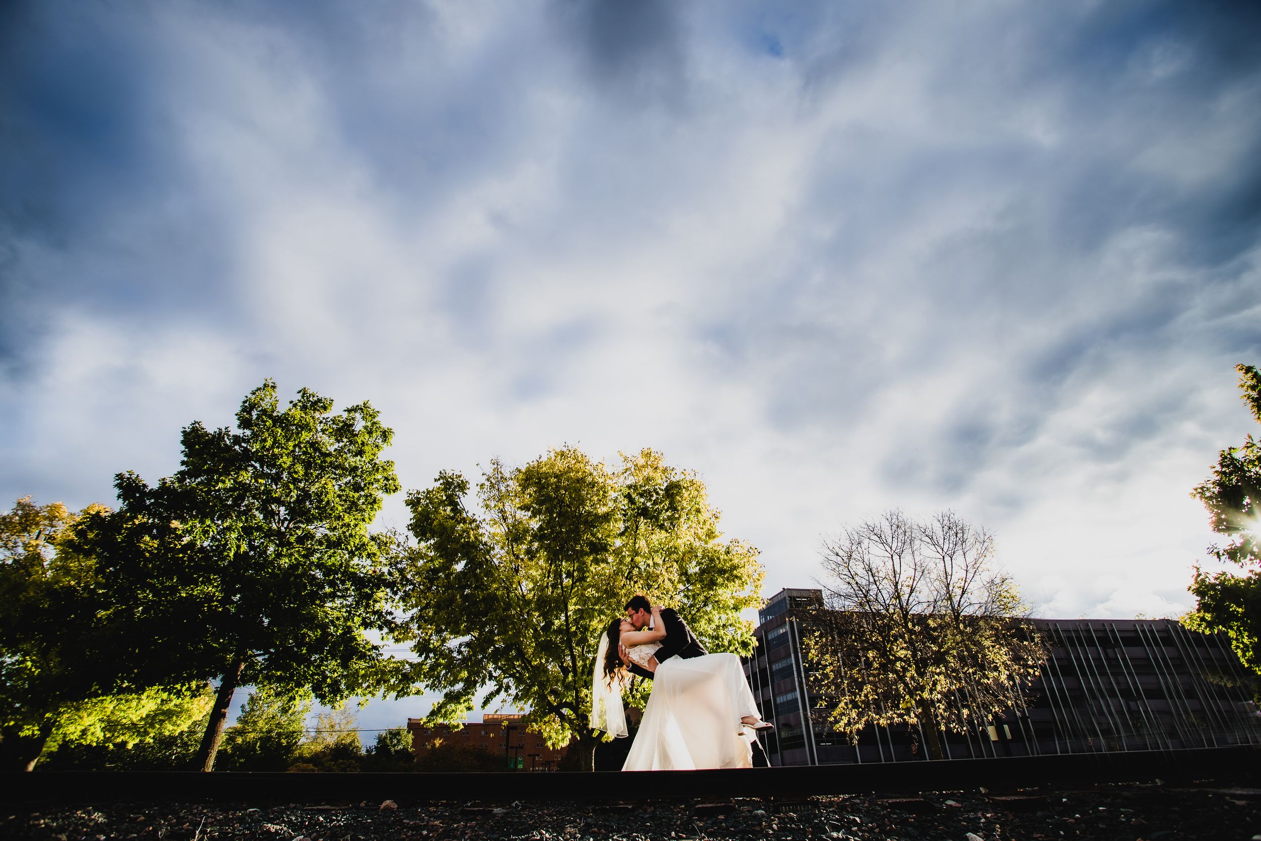 Dramatic wedding portrait with moody sky and rustic barn silhouette.