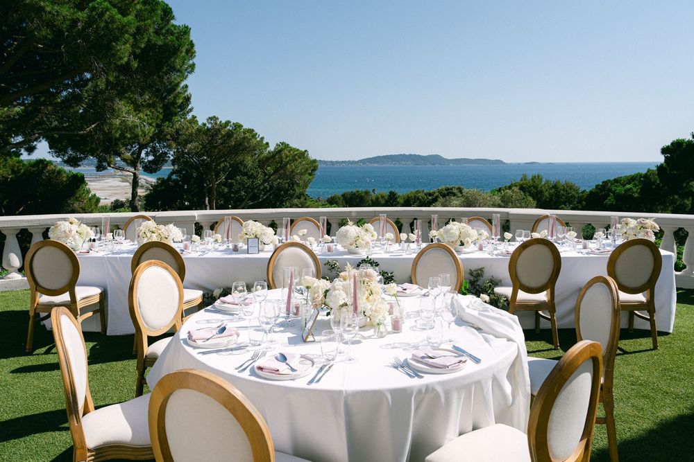 Elegant outdoor wedding reception tables with white linens and gold chairs overlooking a stunning blue sea vista.
