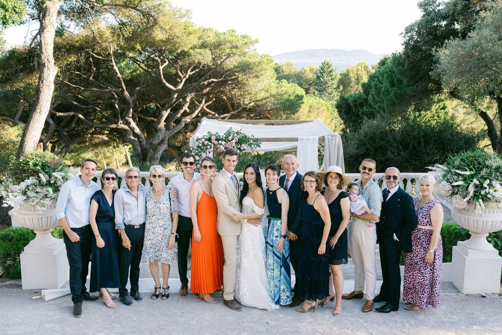 Group of elegantly dressed wedding guests posing together outdoors at a sunny Mediterranean villa celebration.