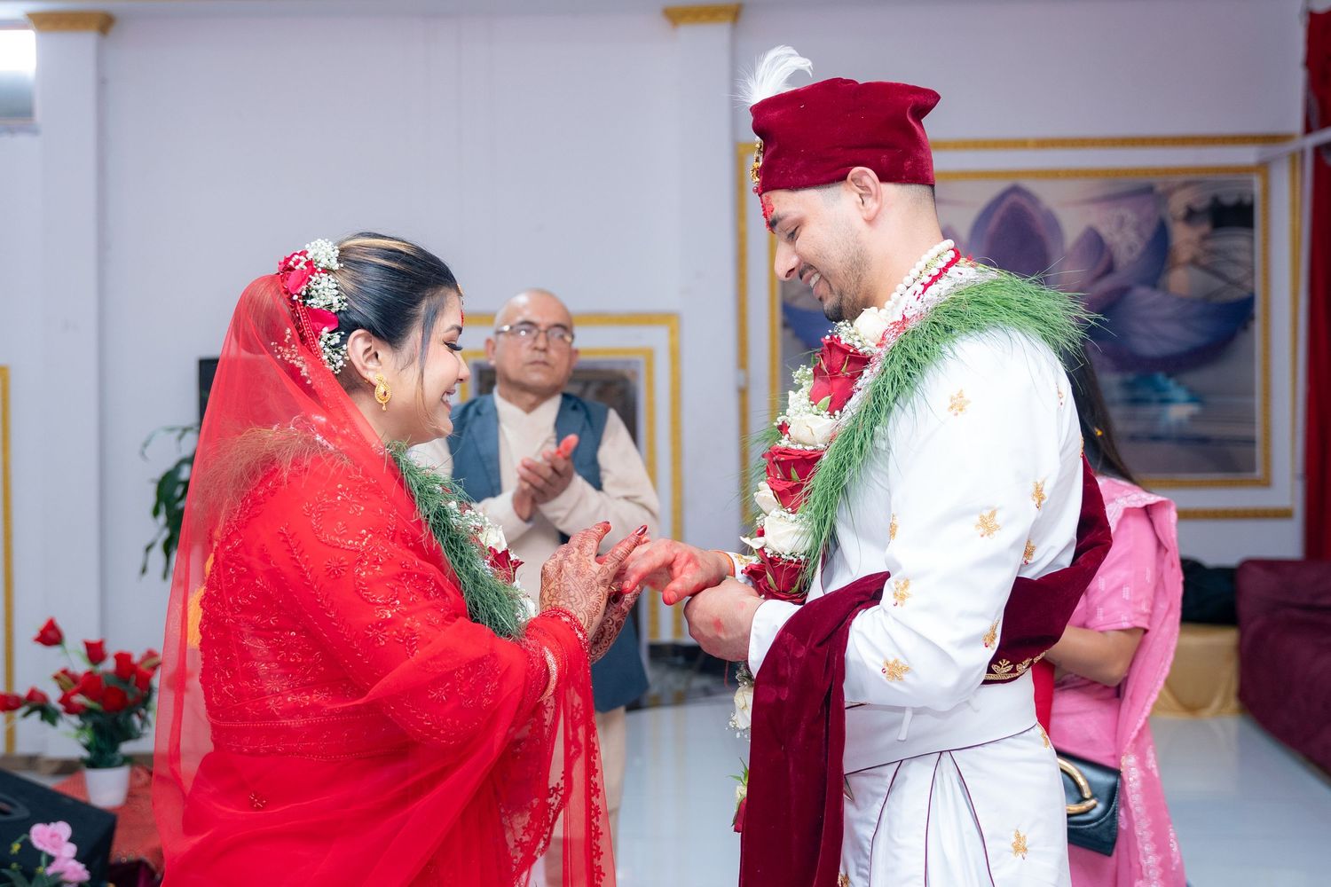 Bride and groom exchanging vows in traditional Nepali wedding ceremony with elder blessing in background.